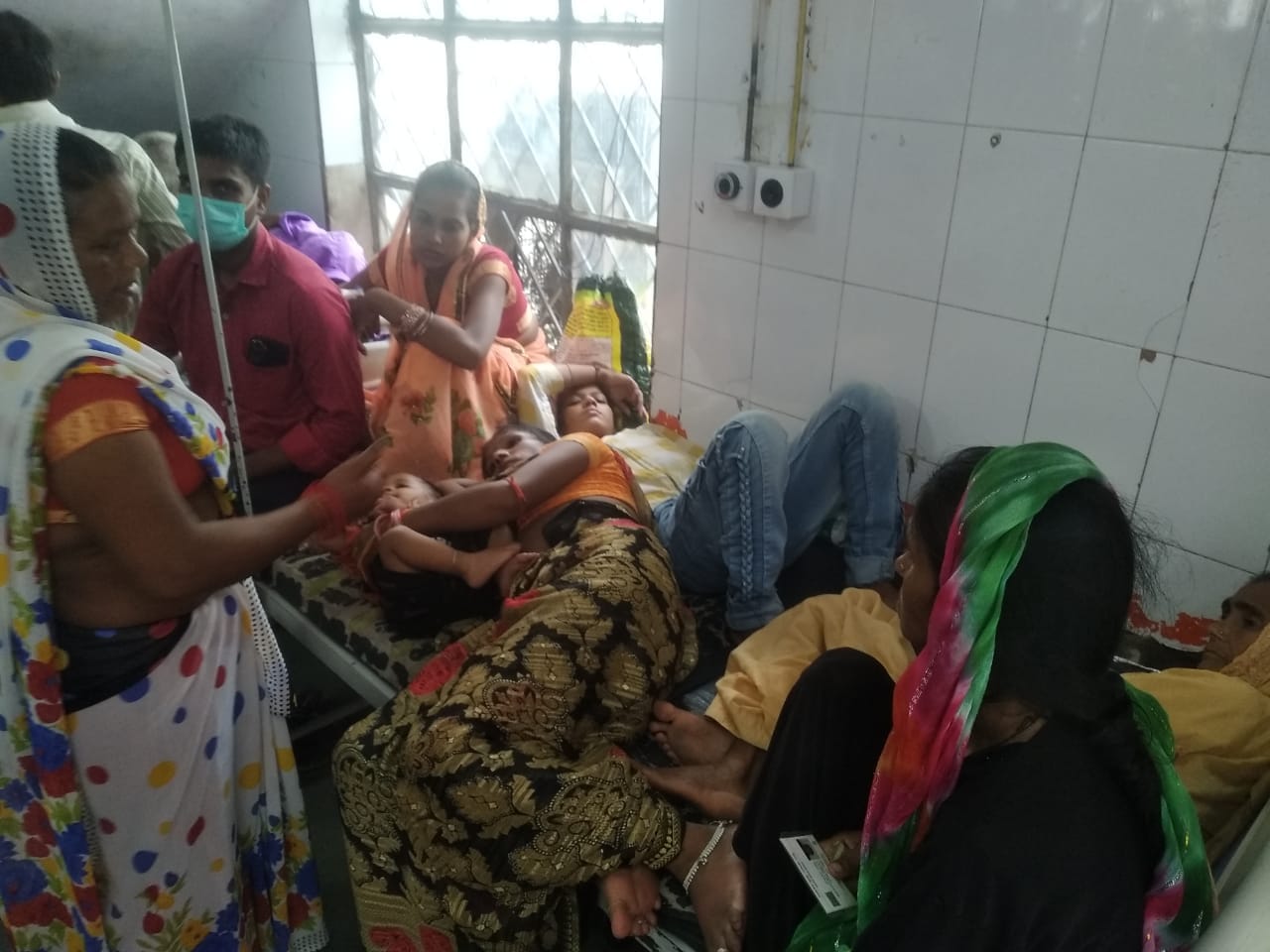 शाहजहांपुर में ट्रामा सेंटर में गर्मी के चलते हाथ में पंखा लिए खड़ी महिला