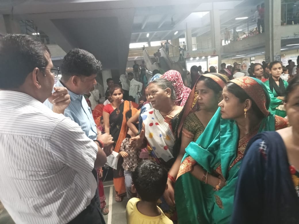 शाहजहांपुर में ट्रामा सेंटर में गर्मी के चलते हाथ में पंखा लिए खड़ी महिला