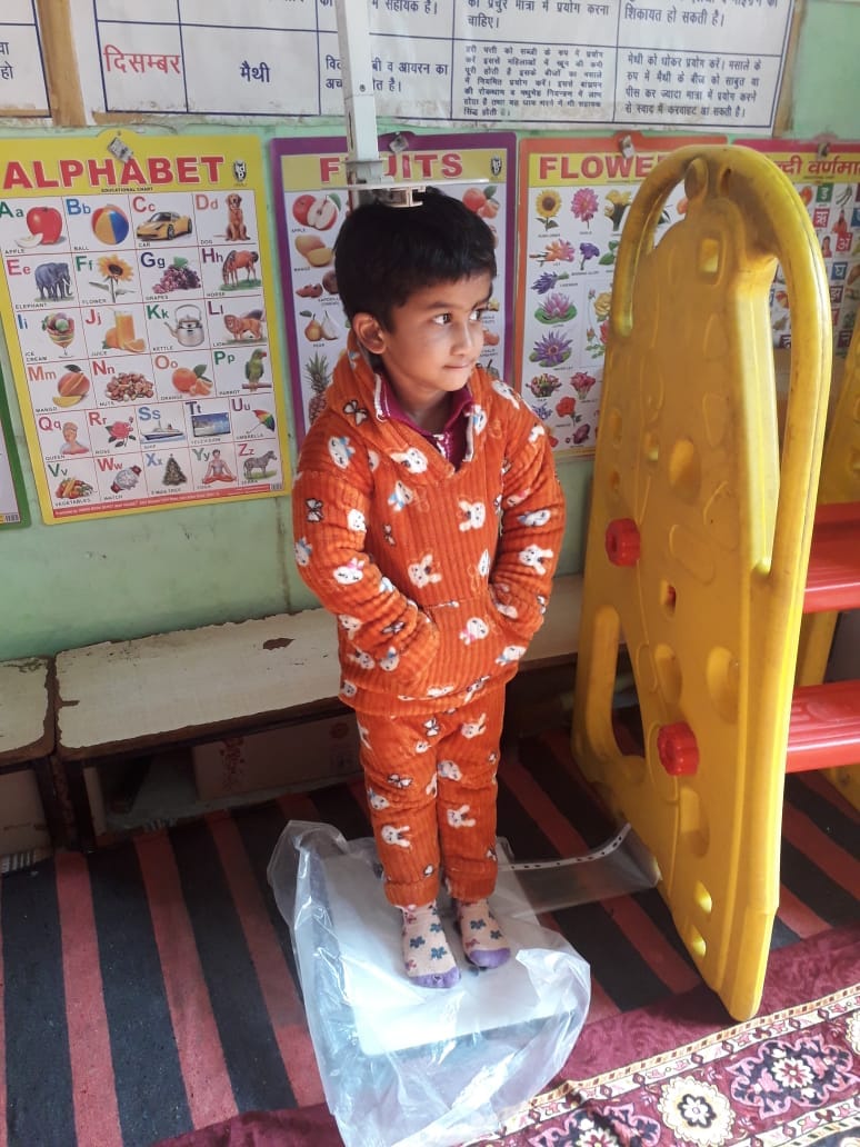 आंगनबाड़ी केंद्र हाथी की कब्र में बच्चा अपना भार नोट करवाता हुआ। संवाद