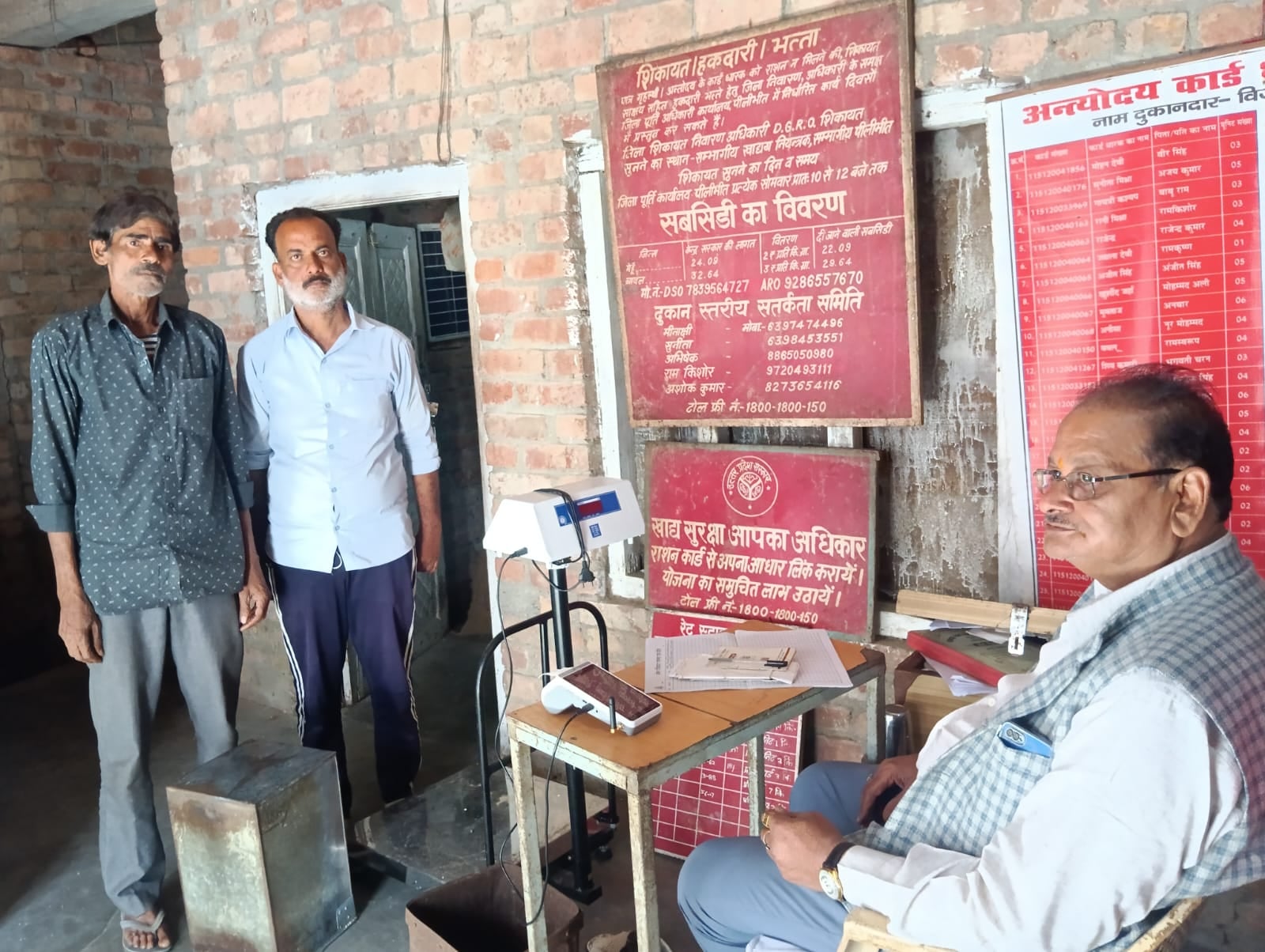 शहर की राशन की दुकान पर मशीन नही चलने से राशन लेने के इंतजार में बैठे लोग । संवाद