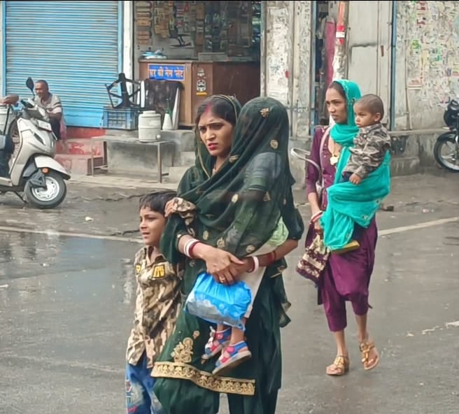 सोनीपत के एटलस रोड पर बूंदाबांदी के बीच स्कूटी पर बारिश से बचने के लिए सिर पर कपड़ा ओढ़े जाते य