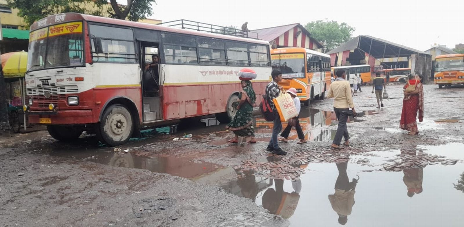 प्राइवेट बस स्टैंड पर कीचड़ से होकर बस चढ़ते यात्री। संवाद