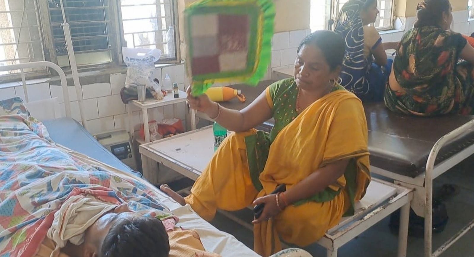 गर्मी से बेहाल मरीज फर्स पर लेटा, पास बैठी महिला। संवाद गर्मी से बेहाल मरीज फर्स पर लेटा, पास बैठी महिला। संवाद