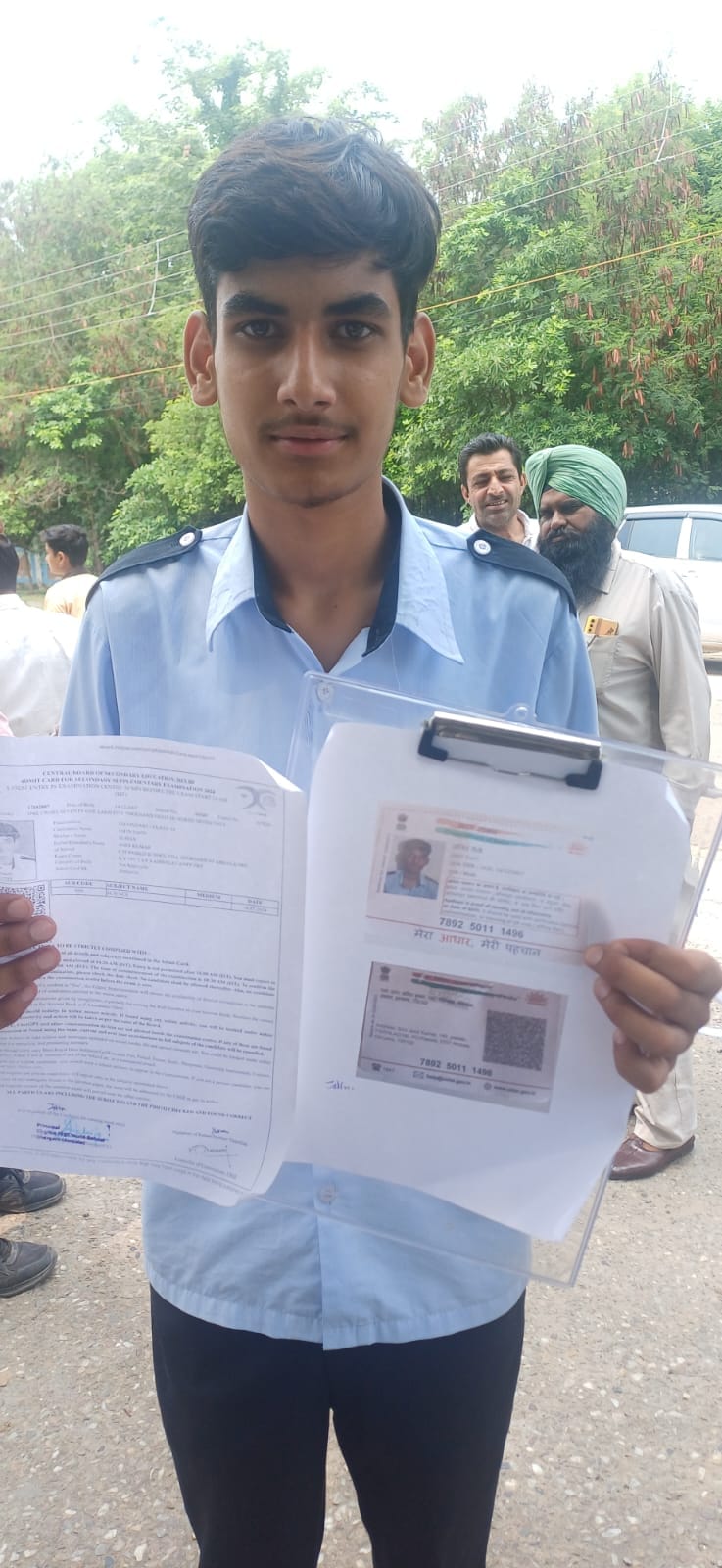 स्कूल के बाहर खडे़ परिक्षार्थी आधार कार्ड की कॉपी दिखाते हुए।