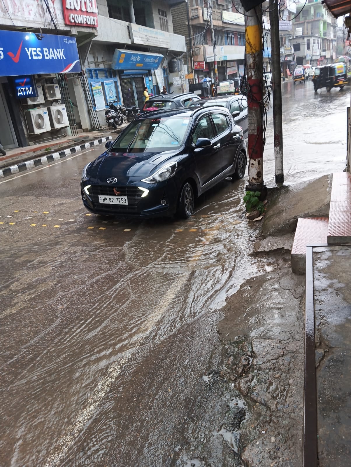 मंडी के चौहाटा बाजार में बारिश के दौरान छाता लेकर अपने गंतव्य की ओर जाते लोग   संवाद