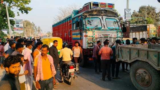 दुर्घटना के बाद बाइक टंकी में लगी आग, घटनास्थल पर मौजूद लोगों की भीड़, ट्रक में फंसी बाइक