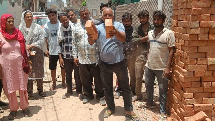 गली निर्माण के लिए आई ईंटों को दिखाते लोग। संवाद
