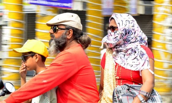 बारिश में छाता लगाकर जाते स्कूटी सवार। संवाद