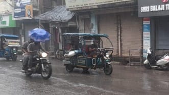 घंटाघर के पास बारिश में सड़क पर भरे पानी में गुजरते वाहन। संवाद
