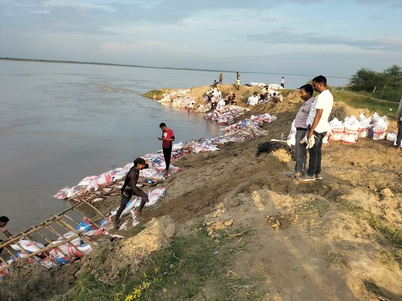 मिट्टी भरी बोरियां डालकर तटबंध कटान रोकने की कोशिश करते मजदूर। संवाद