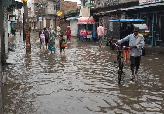जलभराव की वजह से बच्चे को कंधे पर लेकर जाती महिला। संवाद