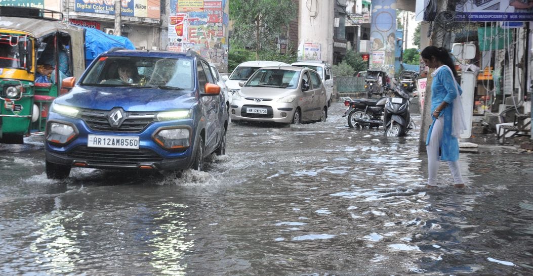 रोहतक स्थित प्रेम नगर मोड़ पर बारिश के बाद हुए जलभराव में से गुजरते वाहन