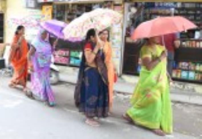 धूप से बचने के लिए छाता लेकर जातीं महिलाएं।
