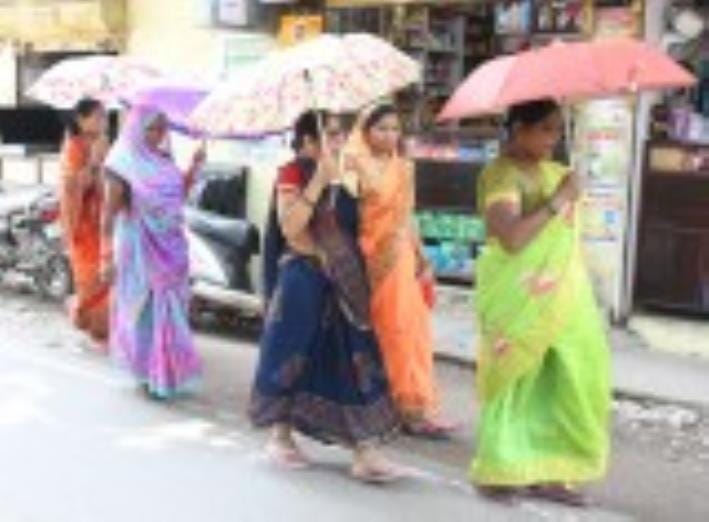 धूप से बचने के लिए छाता लेकर जातीं महिलाएं।
