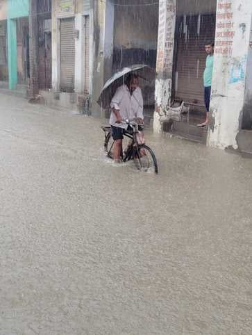 ऊन में  बारिश से  जलभराव के बीच से जाते बाइक  सवार । संवाद