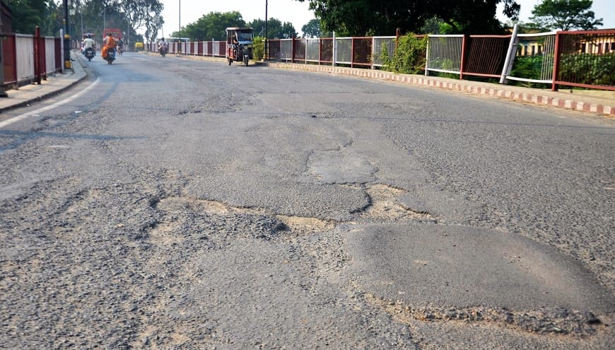 अशफाक नगर चौकी के पास सड़क पर उखड़ी पड़ी बजरी। संवाद