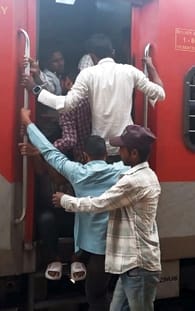शाहजहांपुर रेलवे स्टेशन पर ट्रेन के गेट पर लटक कर जाते यात्री। संवाद
