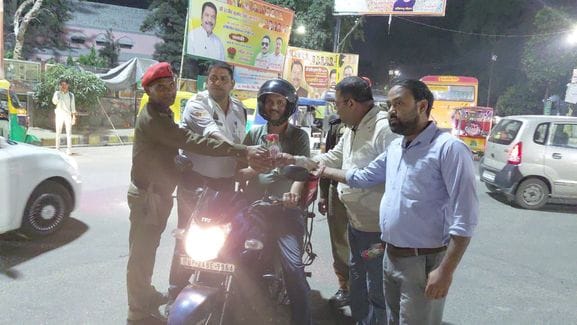 हेलमेट पहने बाइक सवार को फूल देते यातायात कर्मी व समाजसेवी। संवाद