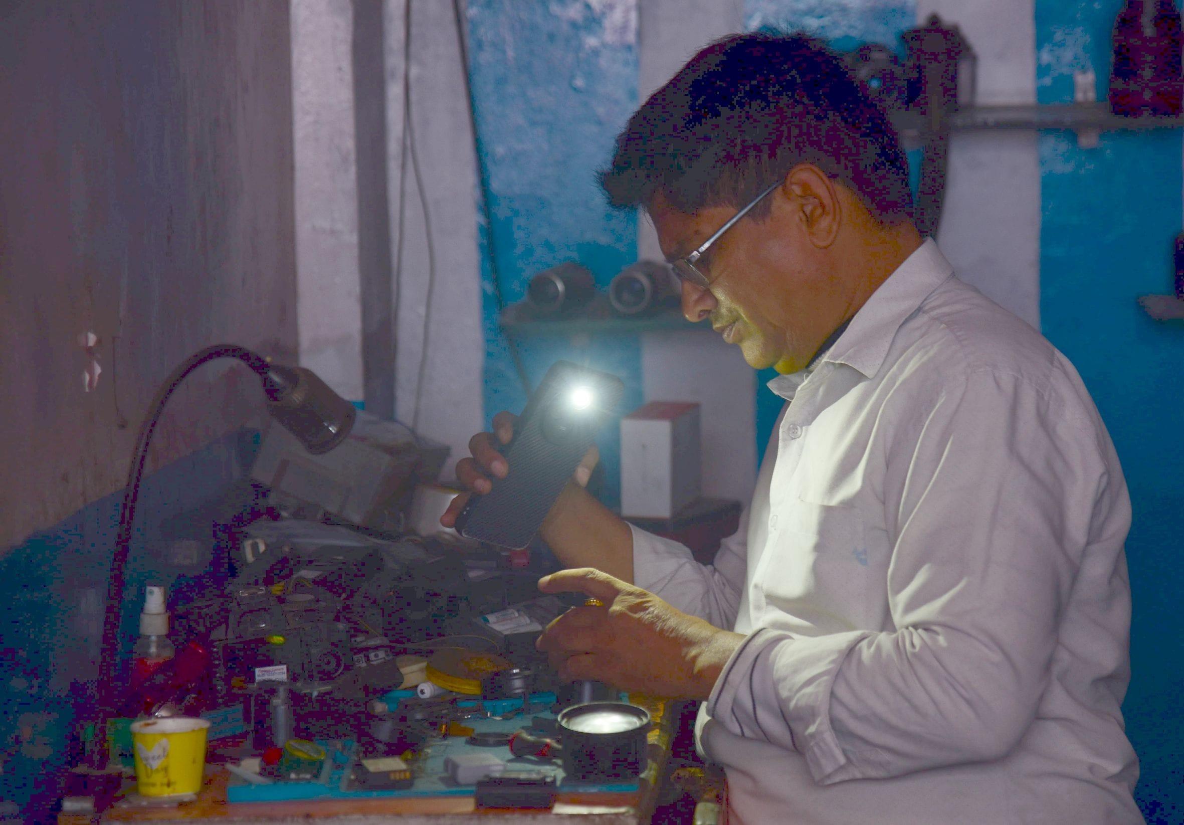 मोबाइल टॉर्च की रोशनी में काम करता दुकानदार और दुकान में सन्नाटा। मोबाइल टॉर्च की रोशनी में काम करता दुकानदार और दुकान में सन्नाटा।