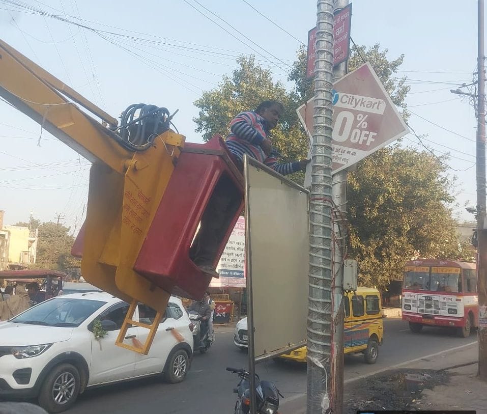 दातागंज तिराहे पर बिजली के खंभें पर लगे फ्लैक्स हटाते कर्मचारी। स्रोत पालिका