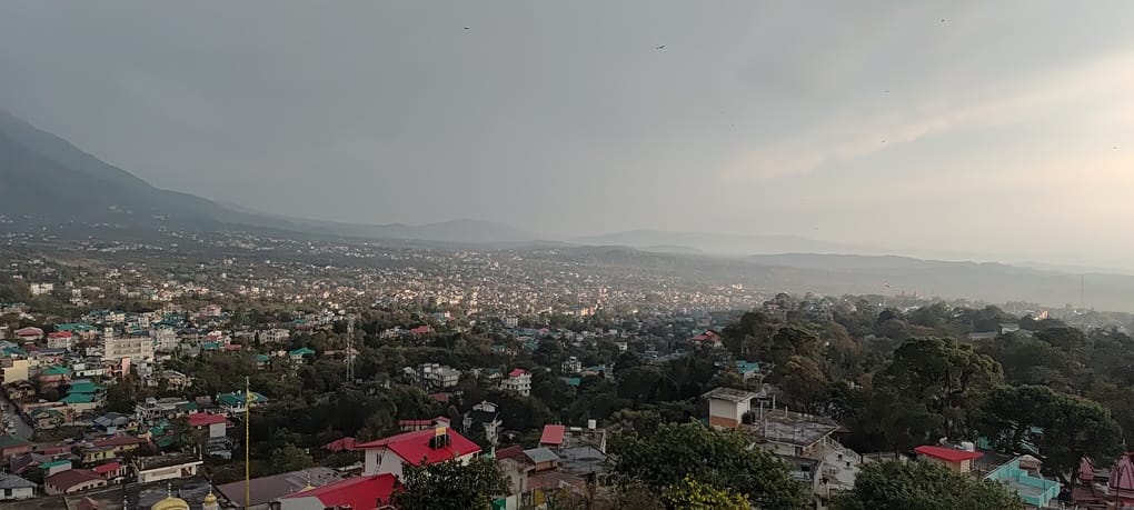 धर्मशाला में दोपहर बाद शुरू हुई बारिश में छाता लिए गंतव्य को जाती महिला। संवाद