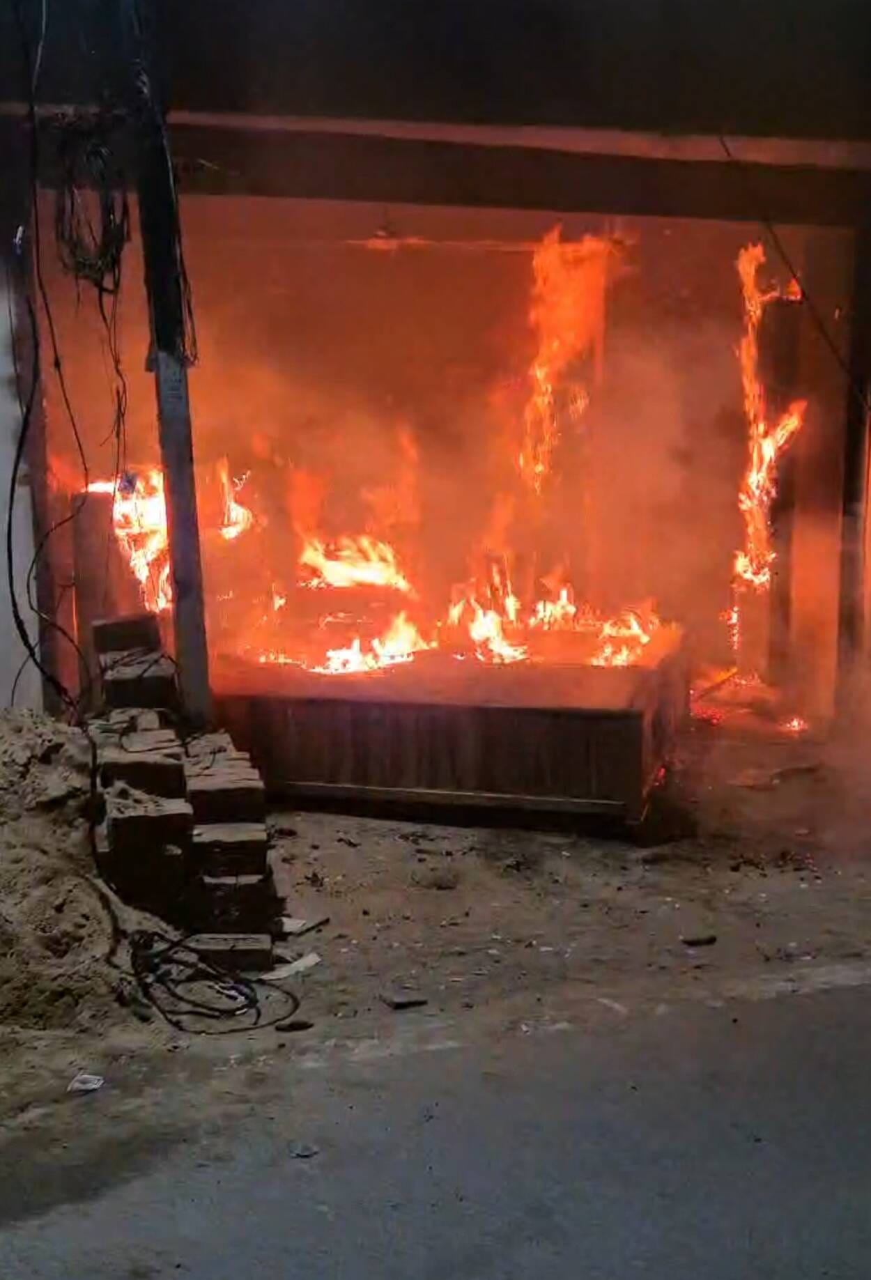 फर्नीचर की दुकान से उठती आग की लपटें व आग बुझाता दमकल कर्मी।