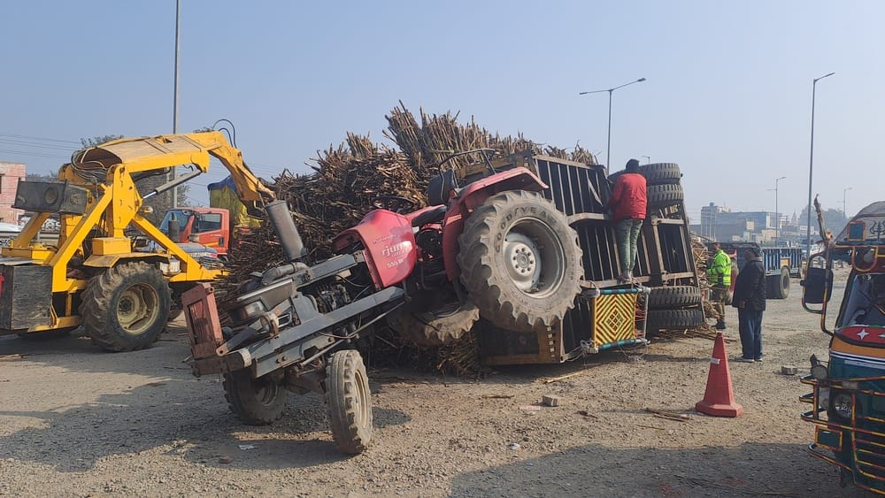 सर्विस लेन पर पलटी गन्ने की ट्राली और आगे से उठा ट्रैक्टर। संवाद सर्विस लेन पर पलटी गन्ने की ट्राली और आगे से उठा ट्रैक्टर। संवाद