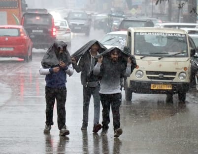 बिजनौर मे बारिश में छाता लगाकर जाते महिला पुरूष। संवाद