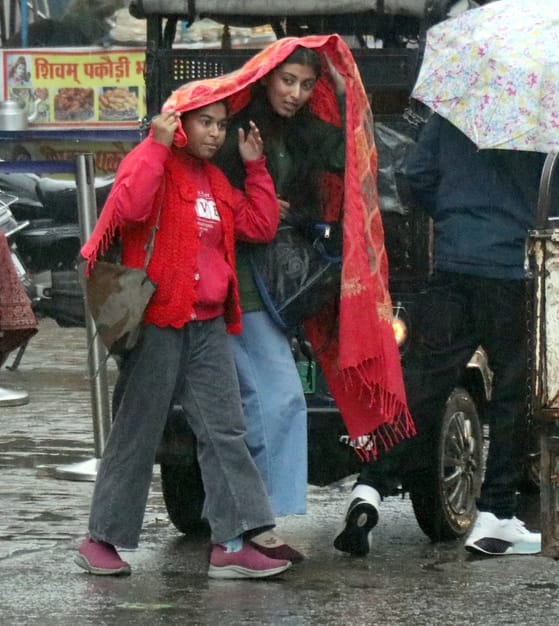 बिजनौर मे बारिश में छाता लगाकर जाते महिला पुरूष। संवाद