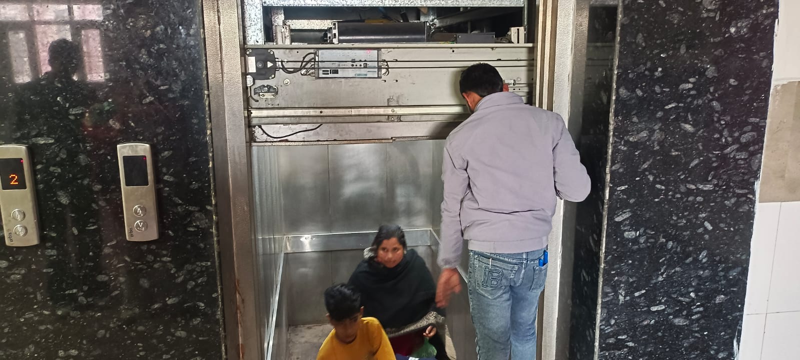 लिफ्ट में फंसे मां-बेटे से फोन पर बात करता कर्मचारी। संवाद लिफ्ट में फंसे मां-बेटे से फोन पर बात करता कर्मचारी। संवाद