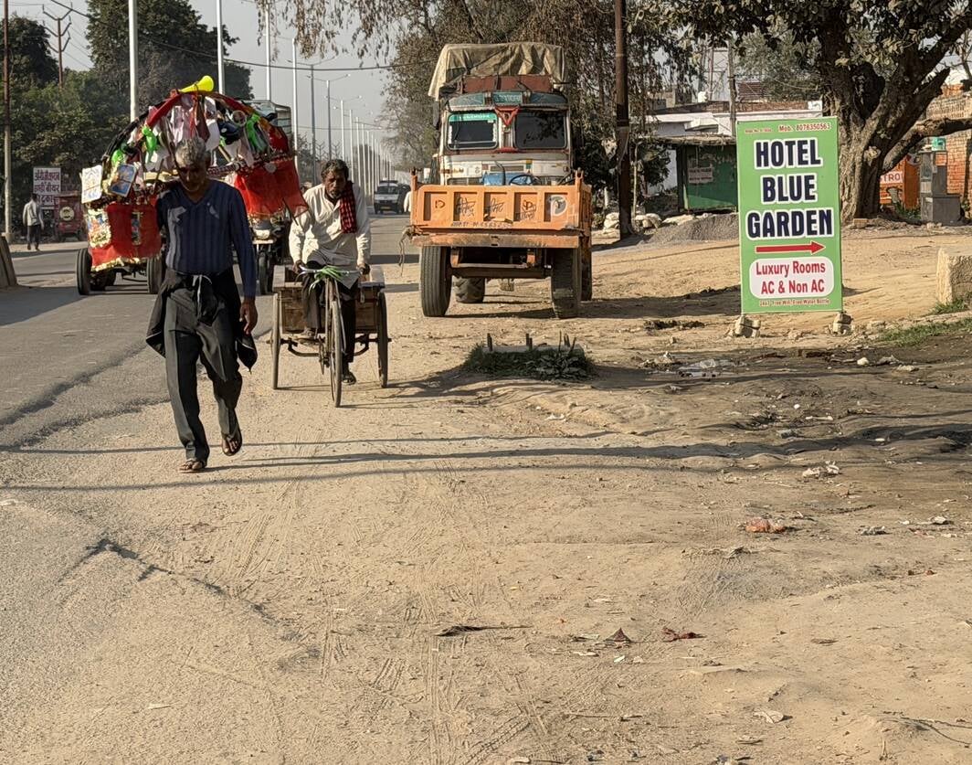 खुर्जा में जंक्शन मार्ग पर गड्डे होने के कारण सड़क किनारे चलते कांवड़िये। संवाद