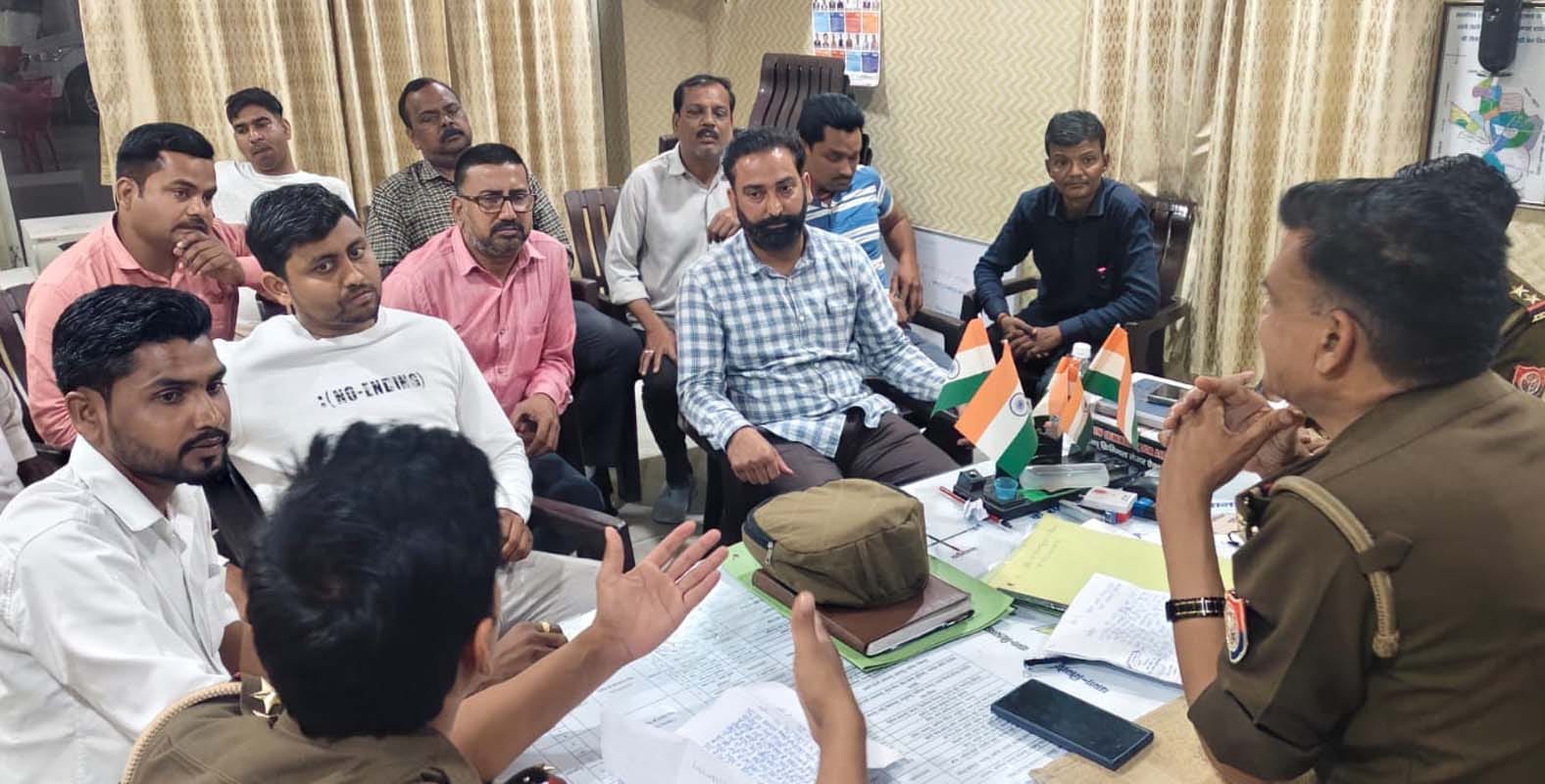 पुवायां थाने के गेट पर धरने पर बैठे व्यापार मंडल पदाधिकारियों को मनाते उपनिरीक्षक। संवाद पुवायां थाने के गेट पर धरने पर बैठे व्यापार मंडल पदाधिकारियों को मनाते उपनिरीक्षक। संवाद