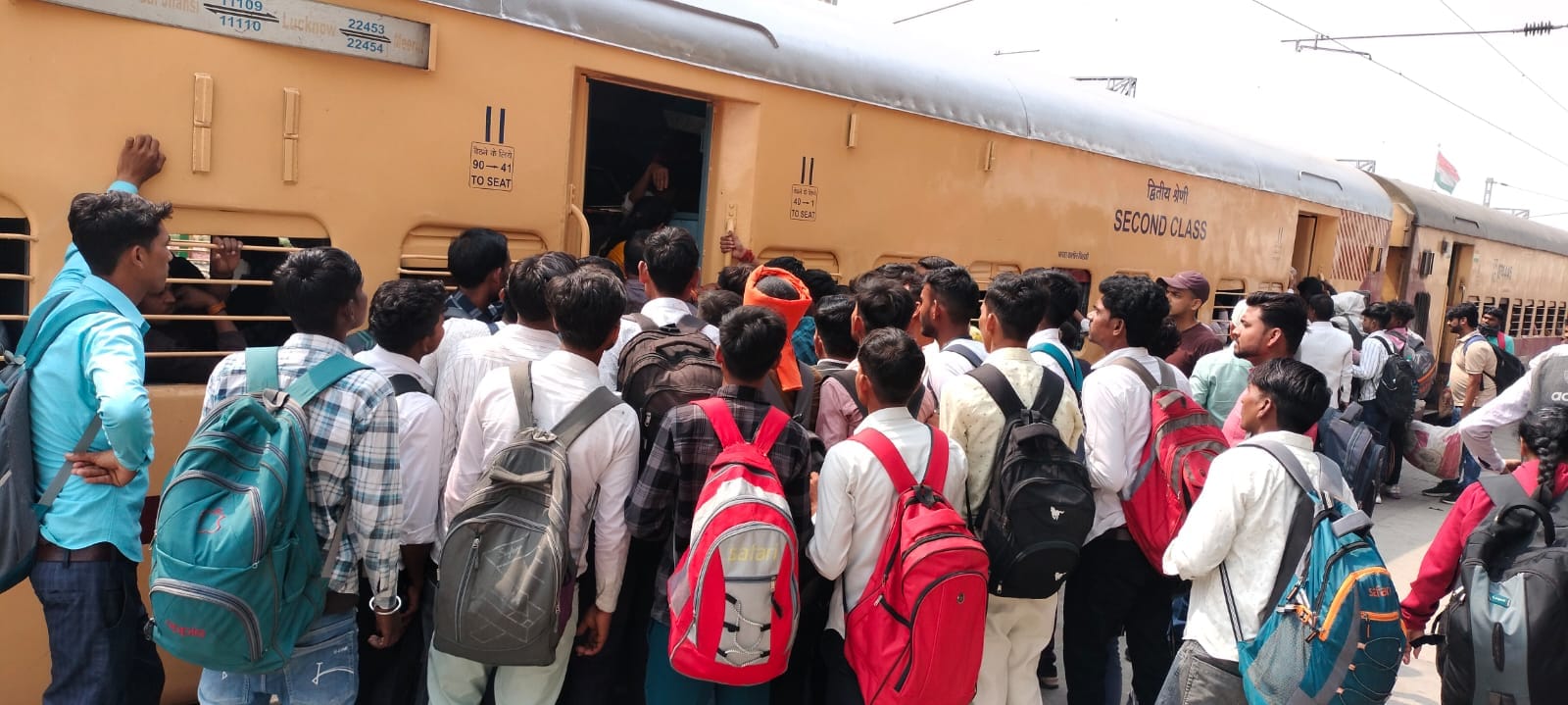 रेलवे स्टेशन पर प्लेटफॉर्म नंबर एक पर जमीन पर  बैठकर ट्रेनों का इंतजार करते यात्री। संवाद