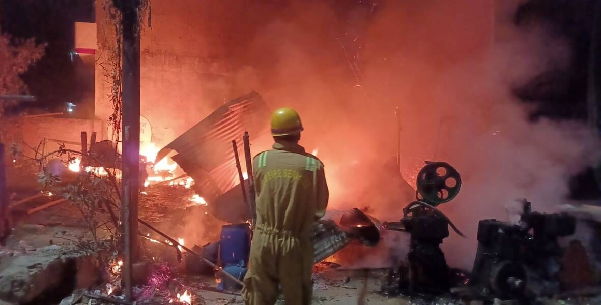 जूस और गद्दे की दुकान से उठतीं लपटें व आग बुझाता दमकल कर्मी।