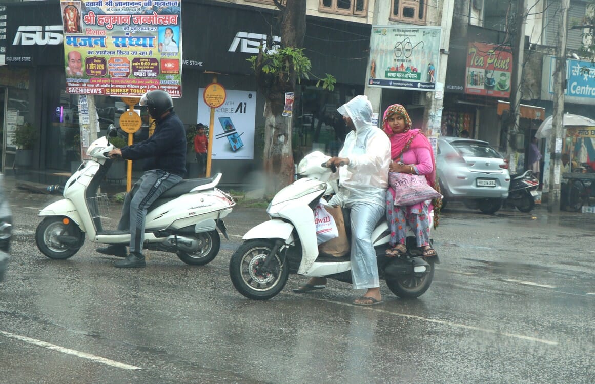 बारिश से बचने के लिए छाता लेकर गुजरते युवक। संवाद