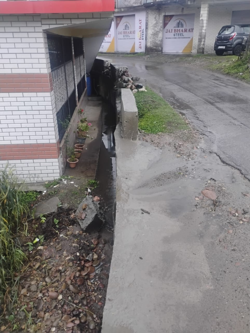 लगदेवी में निकासी नाली के अभाव में सड़क से नीचे गिरते पानी से मकान को खतर। संवाद