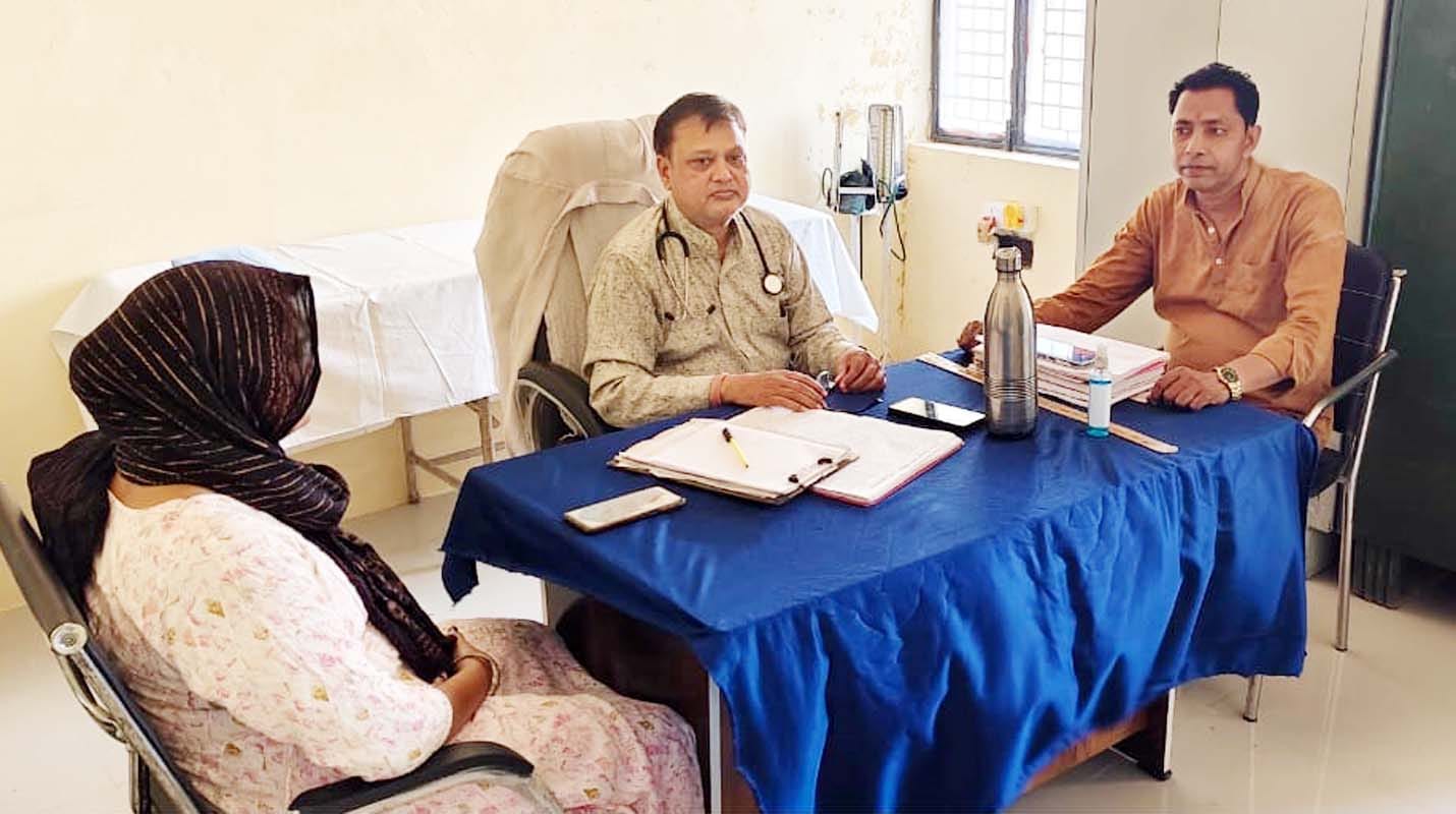 नाहिल पीएचसी पर मेज पर पैर रखकर बैठा किशोर और रोगी देखते फार्मासिस्ट। संवाद