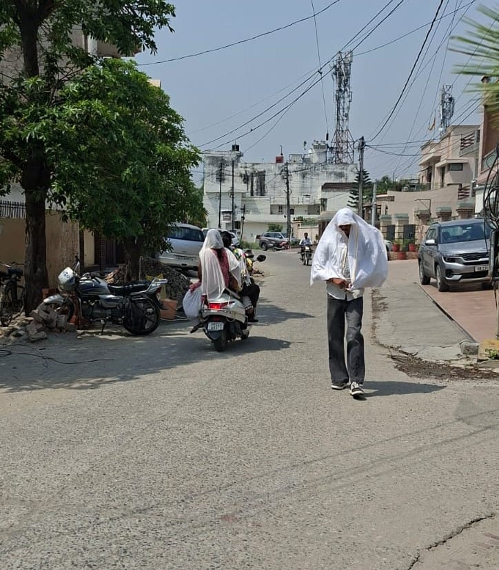 धूप से बचने के लिए मॉडल टाउन की सड़क से छतरी लेकर गुजरती महिला। संवाद