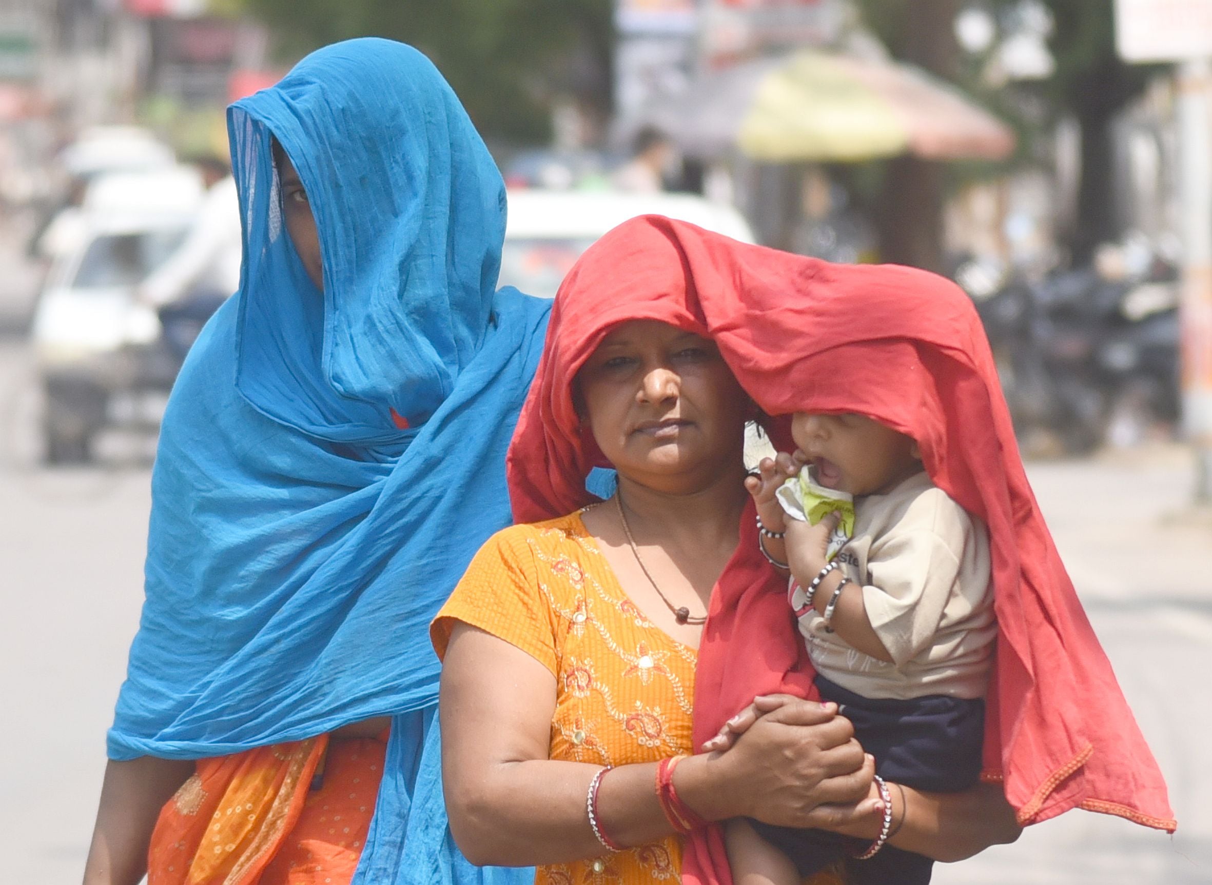 छतरी और दुपट्टे के सहारे धूप से बचाव करते लोग। 