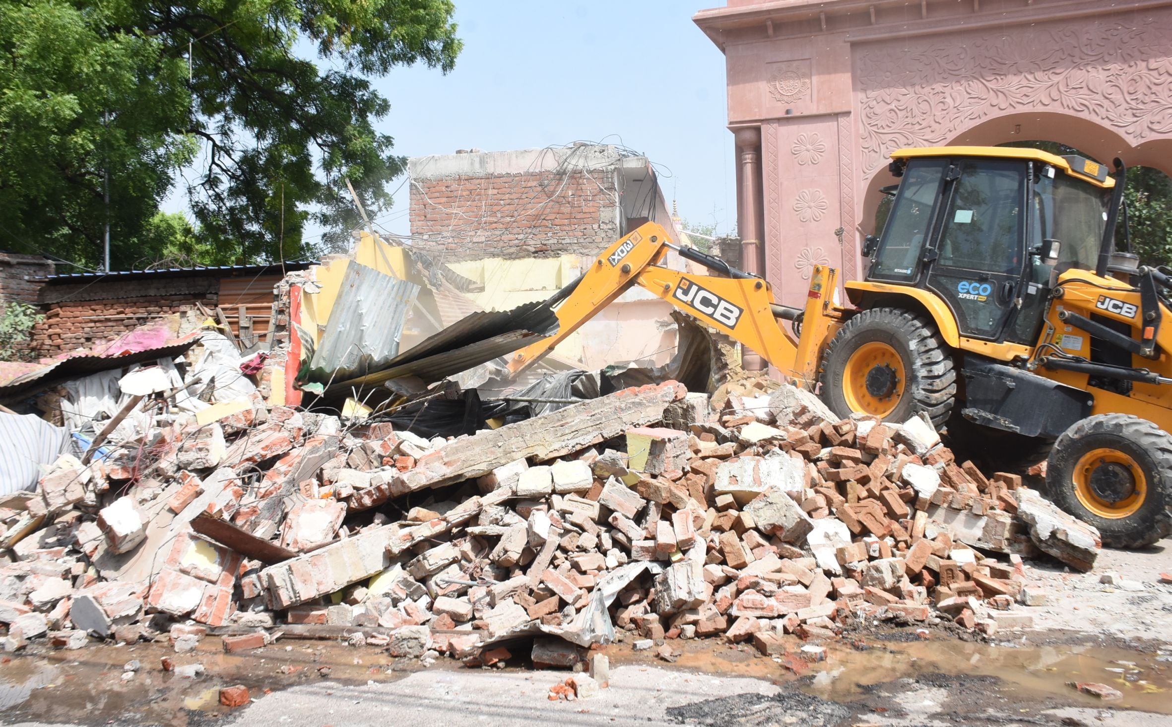 अतिक्रमण ढहाता बुलडोजर और उसे देखते दुकानदार। मौके पर तैनात पुलिस।