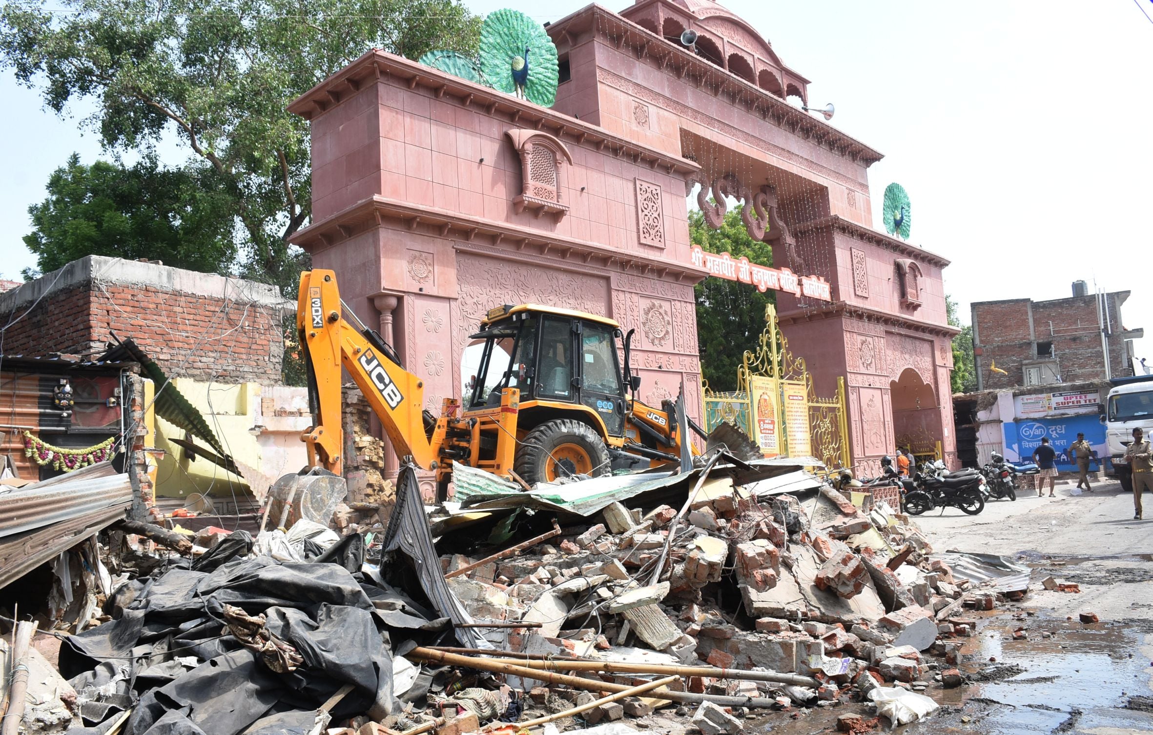 अतिक्रमण ढहाता बुलडोजर और उसे देखते दुकानदार। मौके पर तैनात पुलिस।