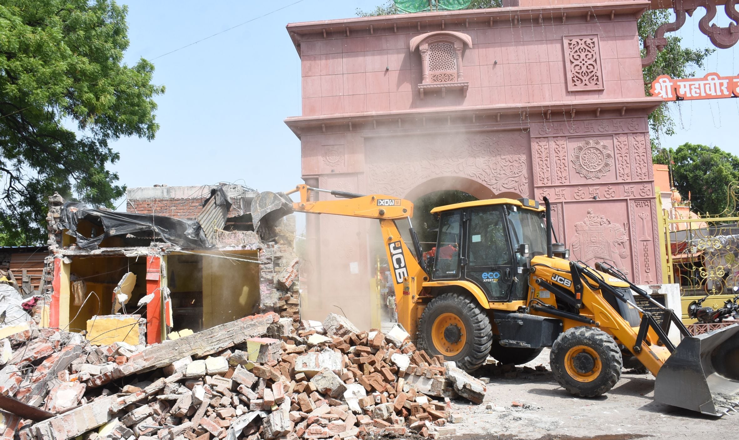 अतिक्रमण ढहाता बुलडोजर और उसे देखते दुकानदार। मौके पर तैनात पुलिस।