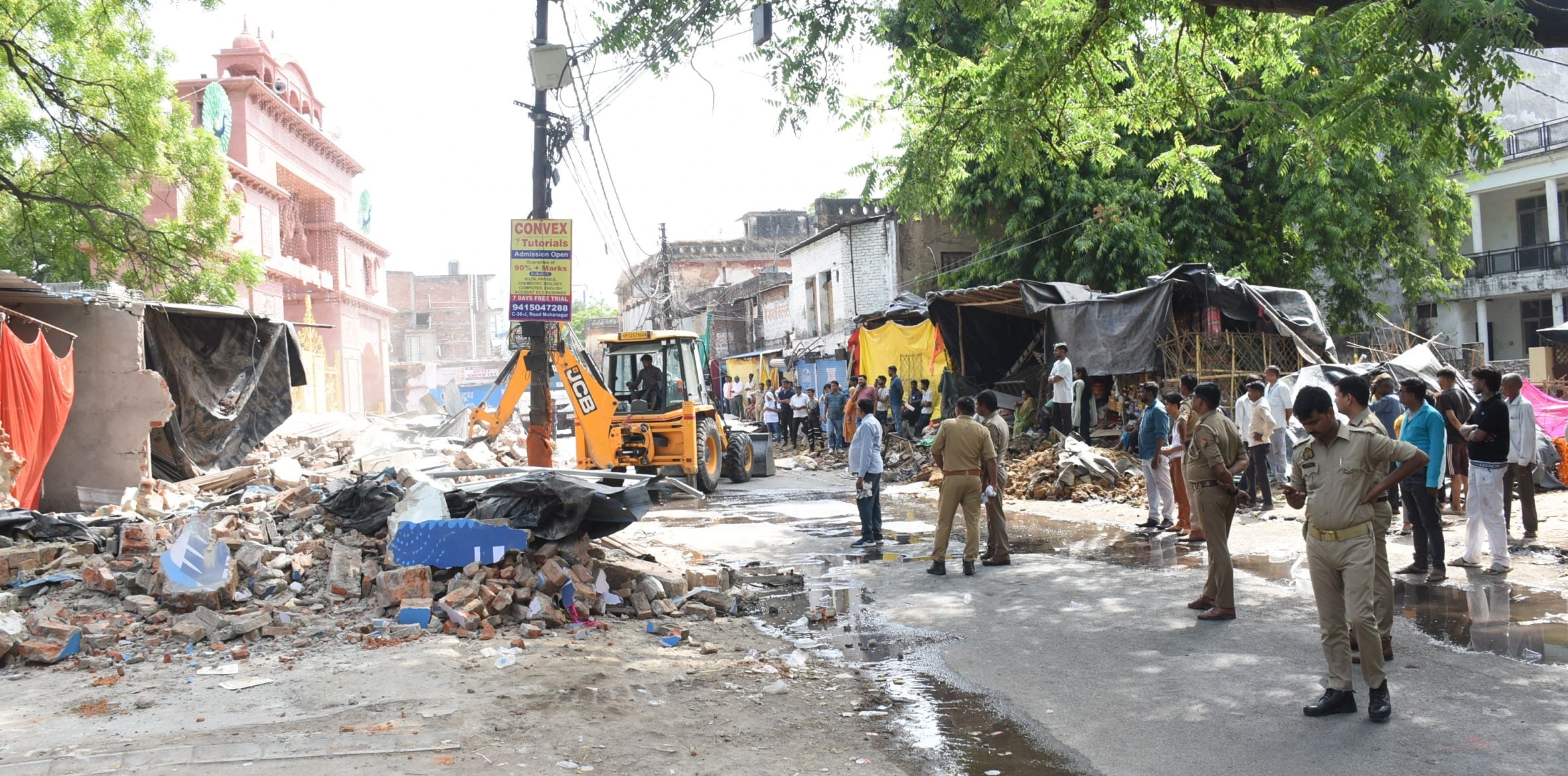 अतिक्रमण ढहाता बुलडोजर और उसे देखते दुकानदार। मौके पर तैनात पुलिस।