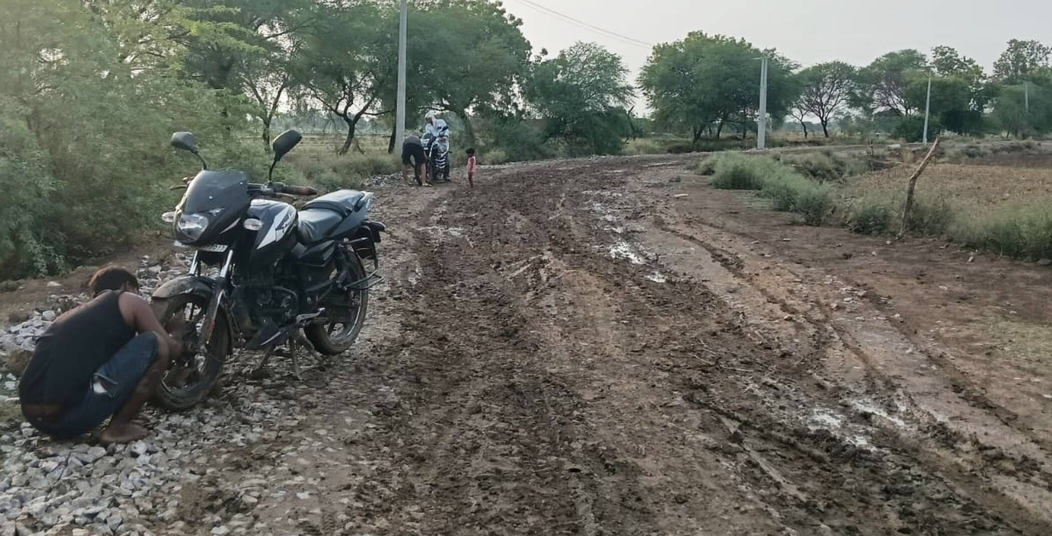फोटो-02-अधबनी सड़क पर पहिए में चिपकी मिट्टी निकालता युवक। संवाद फोटो-02-अधबनी सड़क पर पहिए में चिपकी मिट्टी निकालता युवक। संवाद