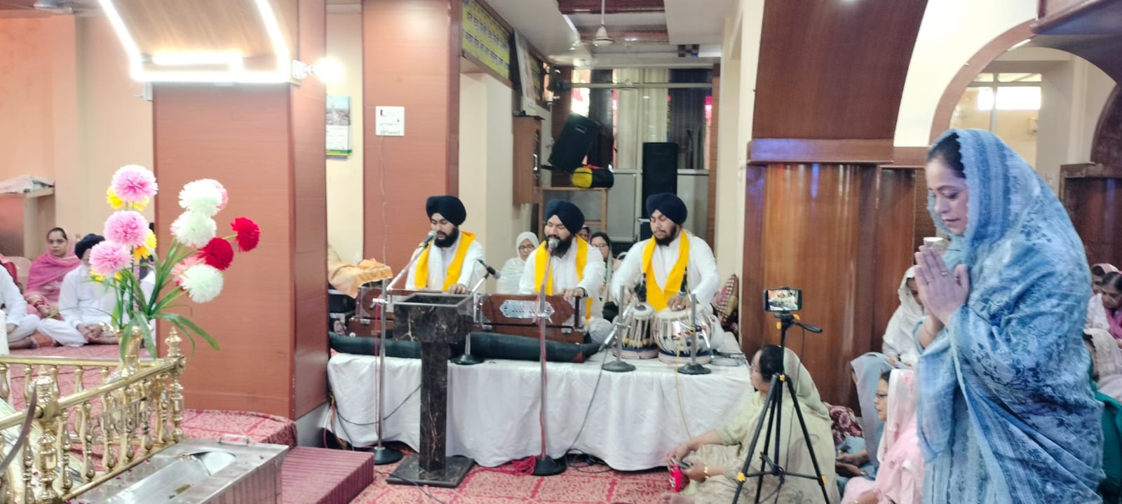गुरुद्वारा श्री गुरु सिंह सभा में गुरुग्रंथ साहिब की पालकी के सामने प्रार्थना करती संगत। संवाद