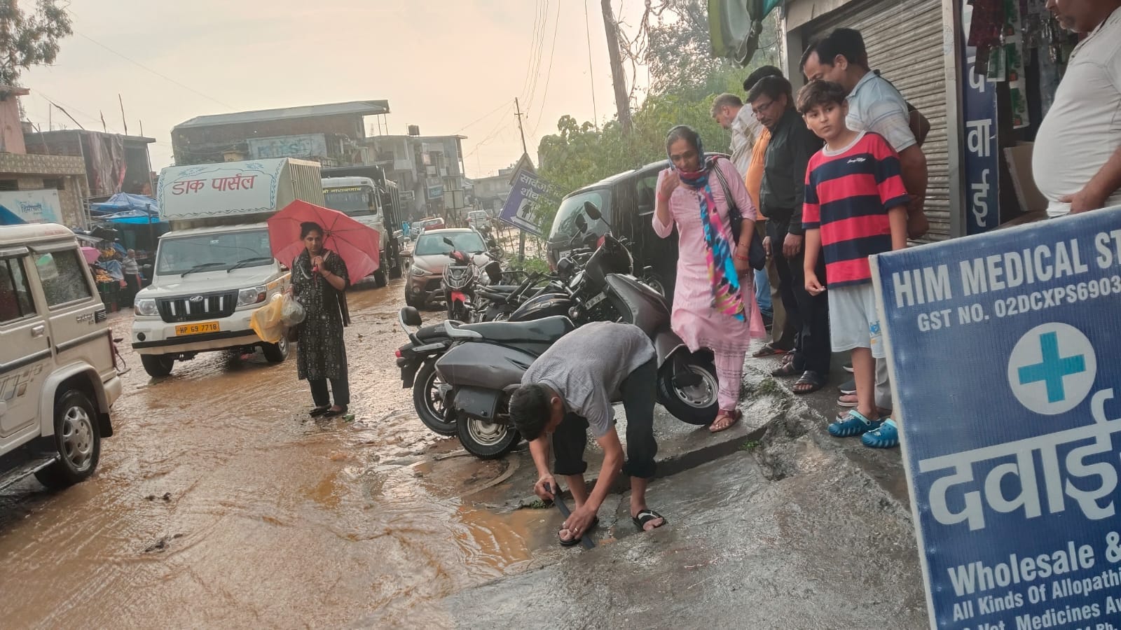 मुख्य बाजार नादौन में बंद निकासी नालियों में फंसे कचरे को डंडे से हटाता दुकानदार। स्रोत जागरूक 