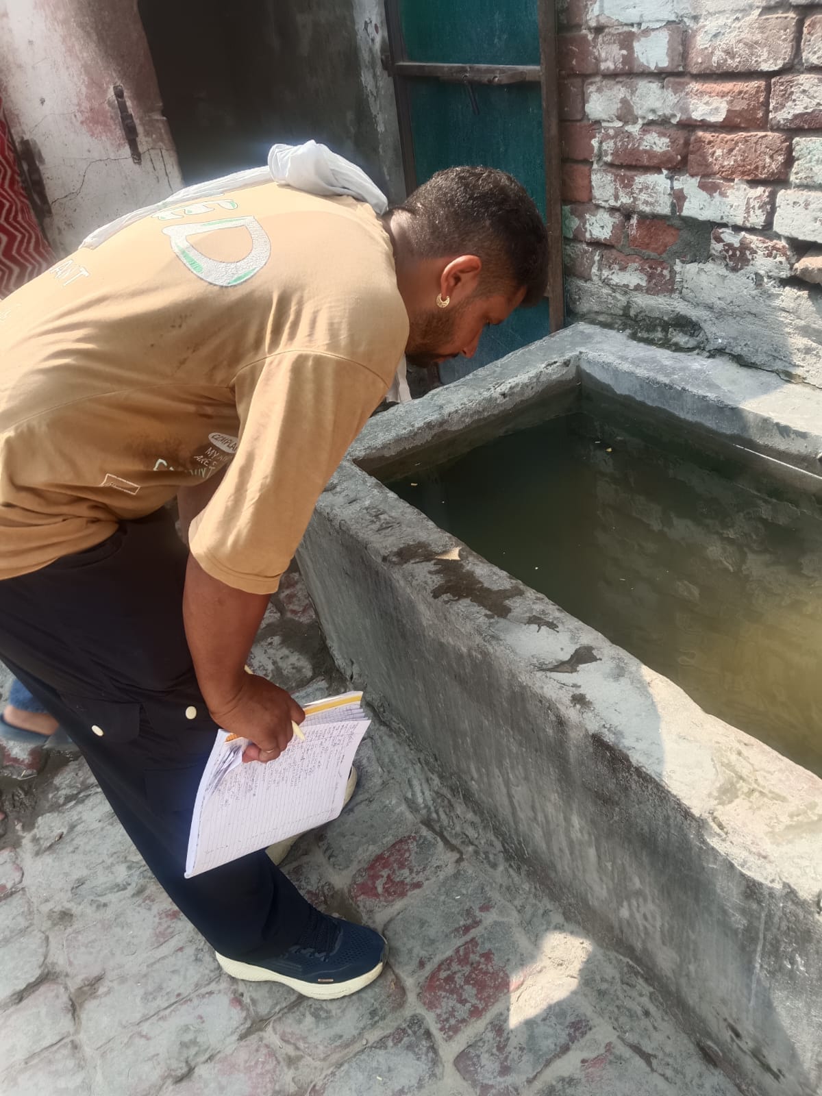 घरों में पानी स्टोरेज टैंक में डेंगू के लारवा की जांच करता कर्मचारी।