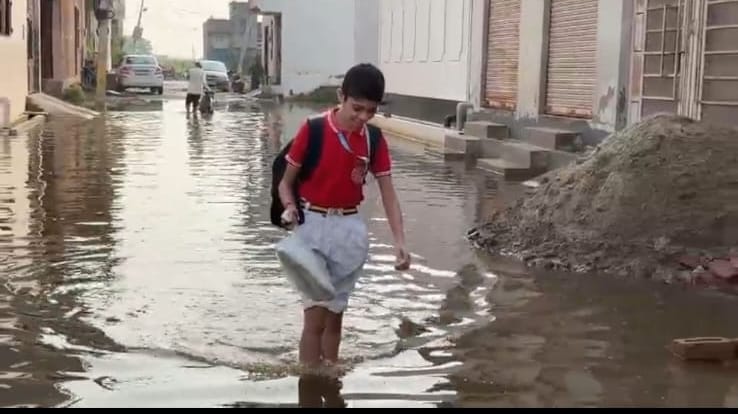 हापुड़ की जय विहार कालोनी में सड़क पर हुए जलभराव में बच्चे को कंधे पर बैठाकर ले जाता युवक। संवाद