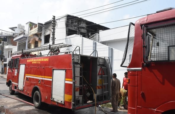 घर की छत पर बने स्टोर रूम से निकलतीं आग की लपटें व आग बुझाते दमकलकर्मी।