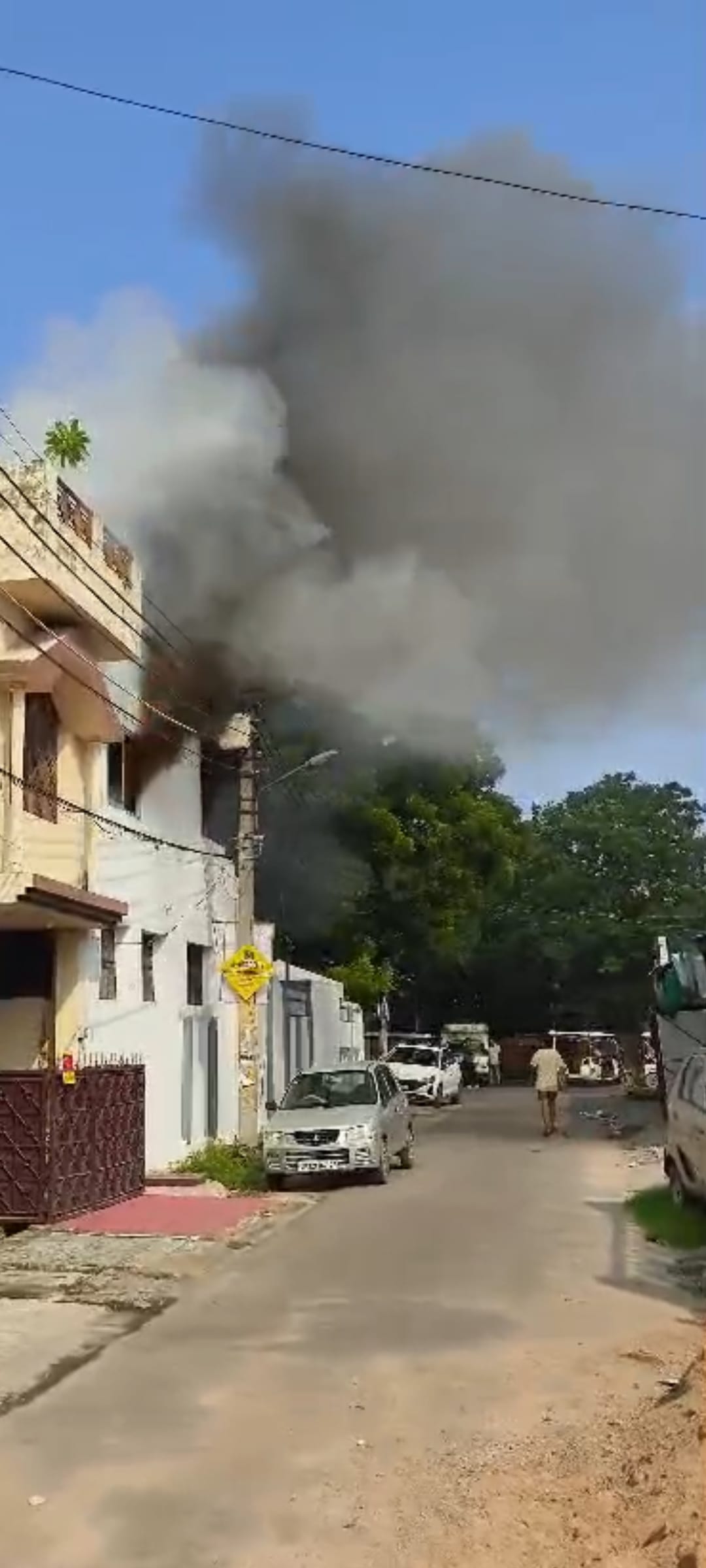 घर की छत पर बने स्टोर रूम से निकलतीं आग की लपटें व आग बुझाते दमकलकर्मी।